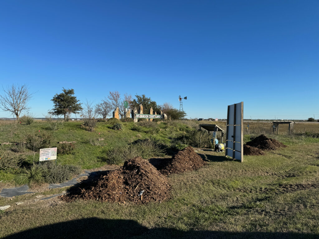 Photo showing piles of mulch with the pollinator garden and Willamson County Landfill sign in the background.